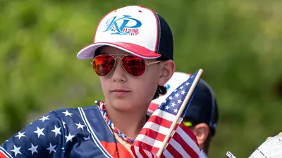 A young athlete in an American flag jersey holds a small flag during the Fourth of July parade in Home, Washington.